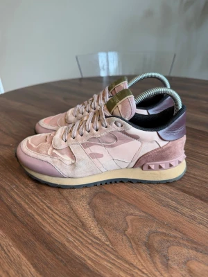 Valentino rosa camo sneakers - Snygga sneakers från Valentino i rosa och beige camo-mönster med detaljer i mocka och läder. Skorna har en unik nitudetalj vid hälen och en beige sula med svarta detaljer. Perfekta för dig som vill sticka ut med stilrena och trendiga sneakers.