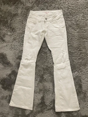 Vita bootcut jeans med hål - Storlek XS 14+ tall. Använda en gång. Vita bootcut jeans med hål på benen. Jeansen har låg midja och utsvängda ben. 