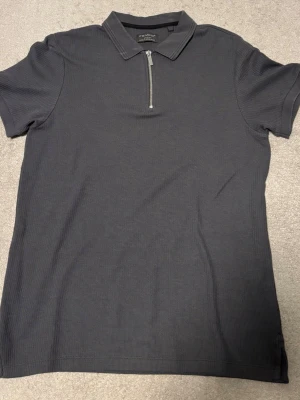 Mörkgrå ribbad topp med half zip - Snygg mörkgrå piké från Primark med kort ärm och klassisk krage. Tröjan har en modern half zip-dragkedja framtill och är tillverkad i ett mjukt, ribbat material som ger en stilren look.