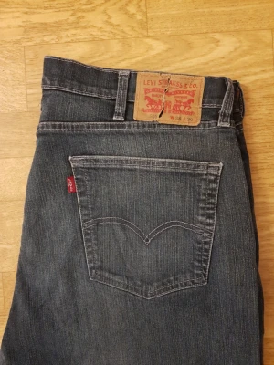Levi's 505 mörk blåa Jeans  - Klassiska blå Levi's 505 jeans i rak modell med fem fickor och tydliga kontrastsömmar. Jeansen har en ikonisk läderpatch bak i midjan och röd Levi's-tagg på bakfickan. Tillverkade i slitstark denim, perfekt för en avslappnad streetstil.