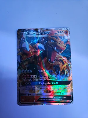 Charizard GX Pokémonkort holografiskt - Säljer ett färgstarkt och holografiskt Charizard GX-kort från Pokémon. Kortet har en cool design med eldiga färger i orange, rött och svart samt glansig yta. Perfekt för samlare eller Pokémon-fans som vill ha något unikt till sin samling.