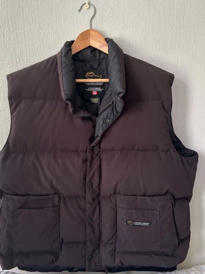 Canada Goose vintage dunväst - Säljer en äkta Canada Goose retro dunväst i mycket bra skick. Västen är sparsamt använd och har inga hål eller större skador.  • Storlek: 2XL (passar även L/XL beroende på hur man vill att den ska sitta) • Passform: Kan bäras oversize på L (skate/loose fit) eller mer normal passform på XL–2XL • Färg: Svart • Fyllning: Äkta dun (väldigt varm och hög kvalitet) • Tillverkad i Kanada  Detta är en äldre/retro modell med mer diskret design (ingen arm patch). Jag bär large och den passar mig, se bild