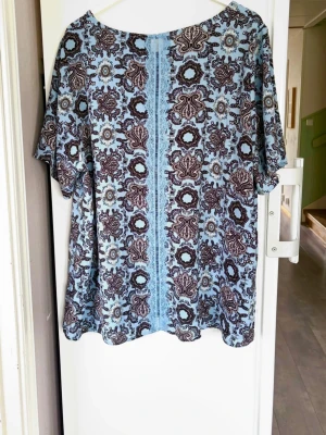 Blommig blå och brun blus från Zizzi - Snygg blus från Zizzi i ljusblått med brunt blommönster. Modellen är lös med korta ärmar och rund halsringning.