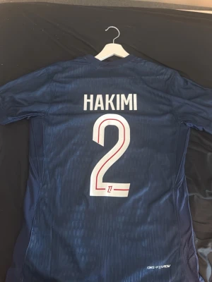 PSG Hakimi matchtröja blå Nike, real madrid valverde vit - Säljer en blå Paris Saint-Germain matchtröja från Nike med Hakimi och nummer 2 på ryggen. Tröjan har korta ärmar, röd och vit detalj i mitten samt Qatar Airways som sponsortryck. Perfekt för fotbollsfans som vill sticka ut på läktaren eller planen. Säljer även en helt ny real tröja från unisport hemsida och det är INTE player version.