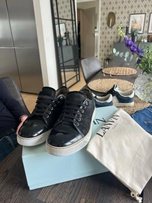 Svarta Lanvin sneakers i mocka och läder - Snygga svarta sneakers från Lanvin med ovandel i mocka och detaljer i blankt läder. Skorna har vita sulor, svarta skosnören och metallfärgade öljetter. Perfekta för dig som gillar stilrena och exklusiva sneakers med lyxig känsla. Ps annan sula i skon som är skönare!