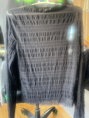 Svart topp med struktur - Säljer en svart långärmad topp från Lindex  med snyggt strukturerat tyg. Toppen är genomskinlig och har en tight passform, perfekt att styla lager på lager. Enkel rund halsringning och stretchigt material.