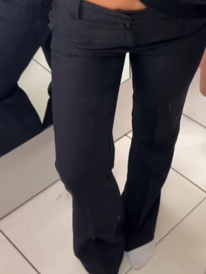 Svarta lågmidjade utsvängda kostymbyxor - Snygga svarta kostymbyxor med utsvängda ben och låg midja. Byxorna har en klassisk look och är perfekta för en stilren outfit. Materialet ser ut att vara mjukt och följsamt, vilket ger en skön passform.