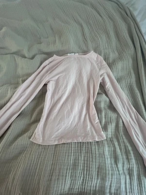 Ljusrosa långärmad topp - En enkel och stilren ljusrosa långärmad topp med rund halsringning. Toppen är figurnära och tillverkad i ett mjukt bomullsmaterial, perfekt att matcha med jeans eller kjol för en clean look.