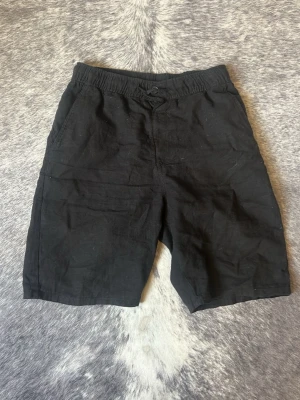 Svarta shorts i bomull - Svarta shorts med elastisk midja och enkel design. Tillverkade i bomull, har fickor fram och en bakficka. Perfekta för varma dagar och en avslappnad stil.