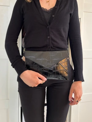 Clutch väska - Med sina mått på 25 x 17 cm är den perfekt stor för det viktigaste – mobil, nycklar och små nödvändigheter – utan att kännas klumpig. Väskan är handgjord i hållbart veganskt läder, vilket ger en mjuk och exklusiv känsla samtidigt som den är ett mer medvetet val.