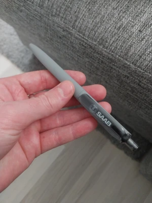 Grå kulspetspenna från SAAB - Säljer en stilren grå kulspetspenna med SAAB-logga på klämman. Pennan har tryckmekanism och är tillverkad i plast. Perfekt att ha i väskan eller på skrivbordet.