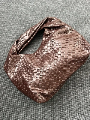 Brun handväska i croco-mönstrat skinn - Säljer en brun handväska med croco-mönstrad yta i konstläder. Väskan har en mjuk, slouchy form och ett kort handtag som gör den enkel att bära i handen eller över axeln. Perfekt accessoar för att lyfta din outfit.