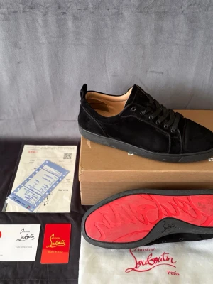 Christian Louboutin - Svarta sneakers i mocka från Christian Louboutin med ikonisk röd sula. Perfekt för dig som vill ha en lyxig och stilren sneaker med exklusiv känsla. Låda medföljer.