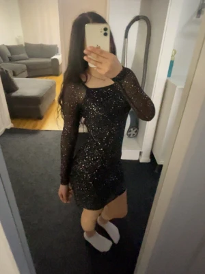 Svart glittrig klänning med meshärmar - Snygg svart klänning med glittrigt tyg och långa meshärmar. Tight passform och kort modell som ger en trendig look. Perfekt för dig som vill sticka ut med lite extra glitter. Rund halsringning och stretchigt material för skön känsla.                                        Funkar både som XS&S 