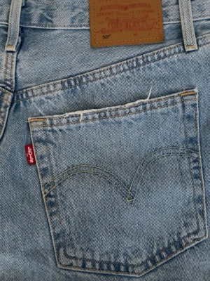 Levi's ljusblå jeansshorts med fransar - Säljer ett par klassiska ljusblå jeansshorts från Levi's med råa fransade kanter och bakfickor med den ikoniska Levi's-sömmen. Shortsen har bälteshällor och en brun läderpatch bak i midjan. Perfekta för sommardagar!