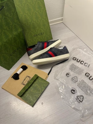 Gucci Ace skor EU41  - Gucci sneakers i mörkgrått monogramtyg med klassiska röda och blå ränder på sidan. Skorna har vit sula med präglad detalj undertill och levereras med originalförpackning, extra skosnören och dustbag. Lyxig och tidlös design som sticker ut. Allt följer med. Helt oanvänd. Storlek 41 EU. Sula 27 cm. Skickar samma dag eller dagen efter. Finns fler bilder :)