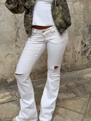 Vita bootcut jeans med hål - Säljer ett par vita bootcut jeans från Gina young 14+, med hål på låret och knät, jeansen har låg midja