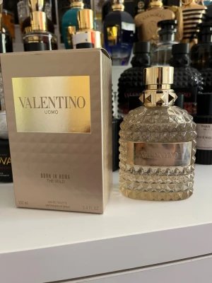 Valentino Uomo Born In Roma The Gold - Lyxig parfym från Valentino, Uomo Born In Roma The Gold. Flaskan är genomskinlig med guldfärgad etikett och lock, dekorerad med nitar och mönstrad glasstruktur. Förpackningen är beige med gulddetaljer och rymmer 100 ml Eau de Toilette. Användt riktigt sällan och består av cirka 95 milliliter kvar om inte mer.