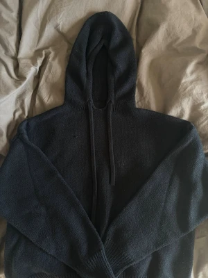 Svart stickad hoodie med huva - En svart stickad hoodie med huva och dragsnören. Materialet är mjukt och sticks inte alls.