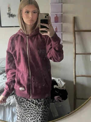 Vinröd hoodie med dragkedja - En vinröd hoodie med dragkedja och huva. Modellen har ribbade muddar vid ärmslut och nederkant samt en ficka framtill. 