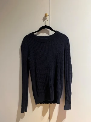 Mörkblå kabelstickad tröja - Snygg mörkblå kabelstickad tröja med rund halsringning och långa ärmar. Tröjan softar till vardagslooken och har ribbade muddar vid ärmslut och nederkant. 
