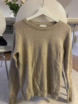 Beige stickad tröja med rund hals - En enkel och stilren beige stickad tröja med rund halsringning och ribbade muddar vid ärmslut och nederkant. Perfekt basplagg i garderoben, passar till det mesta och är lätt att matcha. Strl XS men är lite oversized