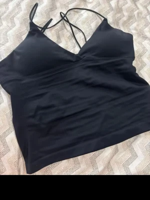 Svart croppad linnetopp med smala band - liknande dfyne Snygg svart croppad linnetopp med tunna axelband och v-ringad hals. Toppen har en enkel och stilren design som passar perfekt till jeans eller kjol. Materialet känns mjukt och stretchigt, vilket gör den bekväm att bära hela dagen.