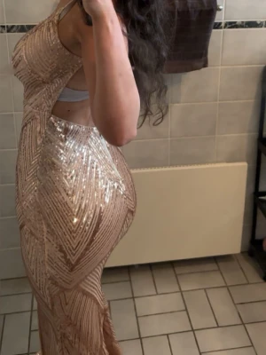 Bal klänning  - Supersnygg långklänning i champagnefärg med glittriga paljetter och geometriskt mönster. Klänningen har smala axelband, djup v-ringning och öppen rygg. Figurnära passform som framhäver siluetten och ger en lyxig känsla. Perfekt för dig som vill sticka ut. Passar xs-s. Endast använd en gång. Den är uppsydd vid bröstet för tyckte den var för v-ringad. Men jag kan sprätta upp ifall man vill det