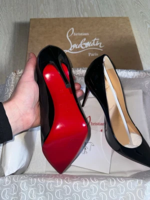 Svarta lackpumps från Louboutin - Säljer ett par ikoniska svarta pumps från Christian Louboutin i glansigt lackläder med den klassiska röda sulan. Spetsig tå och hög klack ger en elegant och edgy look. Skorna levereras med originalkartong och dustbag samt kvitto, ej använda.