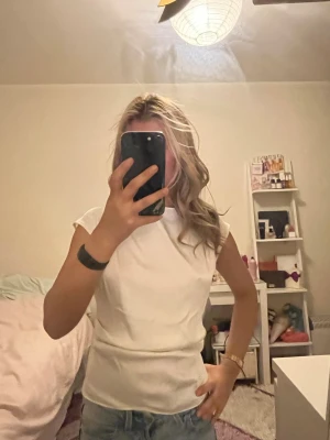 Vit basic t-shirt med rund hals - En enkel och stilren vit t-shirt med rund hals och korta ärmar. T-shirten har en figurnära passform och är gjord i ett mjukt material som passar perfekt till jeans eller shorts. Perfekt för dig som gillar en clean och klassisk look.