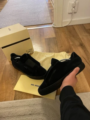 Svarta sneakers från Axel Arigato - Stilrena svarta sneakers från Axel Arigato i mocka med diskret logga på sidan. Skorna har en låg silhuett och svart sula för en clean look. Perfekta för dig som gillar minimalistisk design och vill ha något som funkar till det mesta. storlek 42 dessa säljs ej längre så passa på o köp 