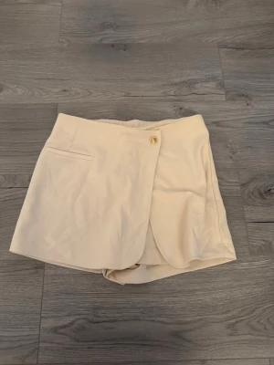 Beige skort  -  beige skort med omlott framtill och en knapp i midjan. 