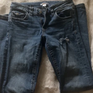 Skitsnygga mörkblå jeans från Gina  - Säljer ett par blå jeans utsvängda och slitning med hål på ena låret. Jeansen har klassisk femficksdesign och dragkedjegylf. Perfekta för en avslappnad och trendig look.