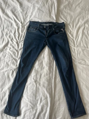Replay anbass hyperflex - Säljer ett par mörkblå replay anbass hyperflex med klassiska fem fickor och snygga sömdetaljer. Jeansen har en slim fit och är tillverkade i stretchigt denim som ger en bekväm passform. Perfekt för dig som gillar en stilren och modern look. Jeansen är 33/32, pytteliten defekt på baksida lapp (se bild) pris kan diskuteras vid snabb affär!🤩