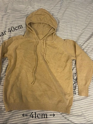 Beige hoodie  - En stilren beige hoodie med huva och dragsko. Hoodien har långa ärmar, ribbade muddar vid ärmslut och nederkant samt en mjuk, slät yta. Perfekt för en avslappnad look och enkel att matcha med andra plagg.