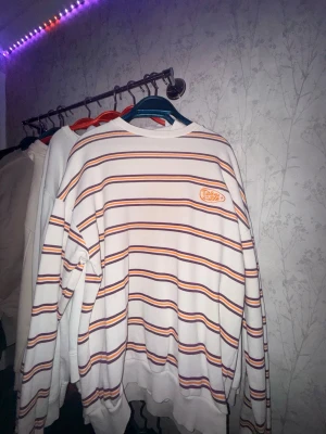 Randig tröja från junkyard - Vit stickad tröja från junkyard. Tröjan har broderad logga på bröstet och ribbade muddar vid hals, ärmslut och nederkant. Oversized passform och mjukt material, perfekt för en avslappnad stil.