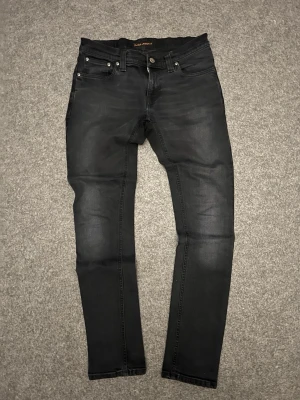 Svarta skinny jeans från Nudie Jeans - Säljer ett par svarta skinny jeans med klassisk femficksdesign från Nudie Jeans. Jeansen har smal passform sober tvätt och silverfärgade nitar. Tillverkade i stretchigt denimtyg för extra komfort. Perfekta för en stilren och modern look.