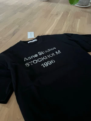 Acne Studios t-shirt - Snygg svart t-shirt från Acne Studios med tryck i vitt på bröstet där det står 'Acne Studios STOCKHOLM 1996'. 