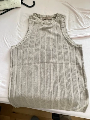 Beige ribbad linnetopp från H&M - Säljer en beige ribbad linnetopp från H&M. Toppen är ärmlös med rund halsringning och har ett snyggt vertikalt ribbat mönster. Perfekt att styla med jeans eller kjol för en clean och enkel look.