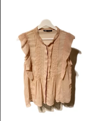 Gammelrosa- Zara blus  - Nu säljer vi en vacker gammelrosa blus från Zara med eleganta volangdetaljer på axlarna som ger ett feminint och stilfullt intryck. Blusen är tillverkad i ett lätt, genomskinligt material som skapar ett luftigt fall och ger plagget en extra exklusiv känsla. Den passar perfekt både till vardag och fest, beroende på hur du stylar den. Modellen är slutsåld i butik och har varit mycket eftertraktad. Ett utmärkt tillfälle att få tag på en populär blus i fint skick.💕