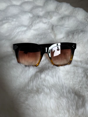 Svarta och bruna fyrkantiga solglasögon - Snygga solglasögon med bred, fyrkantig båge i svart och brun toning. Glasen är lätt tonade i brunt och bågarna har små silvriga detaljer vid hörnen. Perfekta för dig som vill ha en statement-accessoar till sommaren.