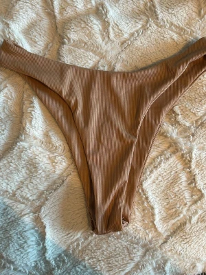 Ribbade bruna bikiniunderdelar - Snygga bikiniunderdelar i ribbat material med hög midja och v-formad skärning framtill. Färgen är en varm brun nyans som ger en trendig look. Perfekt för dig som vill ha en stilren och enkel bikiniunderdel. Materialet känns mjukt och följsamt mot huden.