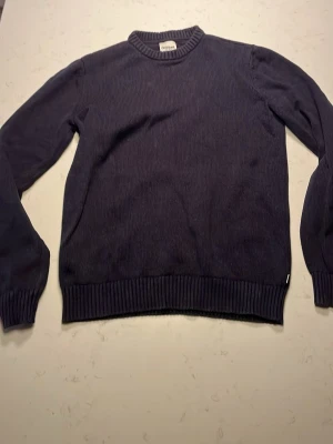 Mörkblå stickad tröja från Dobber - Klassisk mörkblå stickad tröja från Dobber med rund halsringning och ribbade muddar vid ärmslut och nederkant. Tröjan är enkel och stilren, perfekt för lager på lager och passar till det mesta. Materialet känns mjukt och bekvämt.