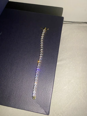 Guldarmband med glittrande stenar - Snyggt armband i guldton med runda, gnistrande stenar längs hela bandet. Klassisk och stilren design som ger en lyxig känsla. Perfekt accessoar för att lyfta din outfit med extra bling.