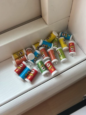 Pringles burk-berlocker  - Flera små berlocker formade som Pringles-burkar i olika färger: röd, gul, blå, grön och orange. Perfekta att använda till smycken, nyckelringar eller som dekoration. Tillverkade i plast med metallögla för enkel fastsättning.