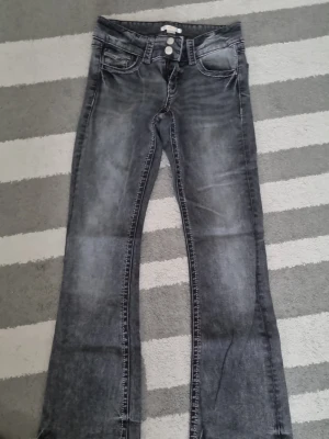 Grå bootcut jeans med tvättad look - Snygga grå jeans med bootcut passform och tvättad effekt. Jeansen har klassisk femficksdesign och kontrastsömmar. Perfekta för dig som gillar en avslappnad men trendig stil. Materialet är denim i bomull.