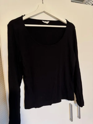 Svart långärmad topp med rund hals - Stl. XL. En enkel och stilren svart långärmad topp med rund halsringning. Perfekt att matcha med jeans eller kjol för en clean look. Materialet känns mjukt och stretchigt, vilket gör den bekväm att bära hela dagen.