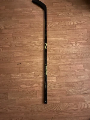 Hockeyklubba - Säljer en svart hockeyklubba med gula detaljer. Klubban är tillverkad i kompositmaterial och har en klassisk böjd bladform. Perfekt för dig som gillar ishockey och vill ha en lätt och stabil klubba. Säljer den för att jag skada mig och kunde aldrig använda den och nu har jag växt ut den. 