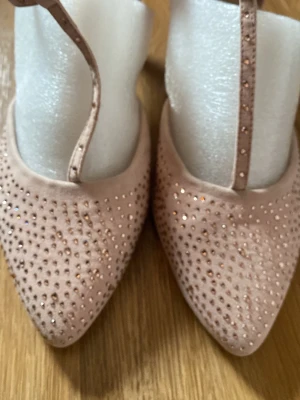 Rosa ballerinaskor med strassdetaljer - Säljer ett par ljusrosa klackar med spetsig tå och tunna remmar. Skorna är täckta med små glittriga strass och har en sammetsliknande yta som ger en lyxig känsla. Perfekta för dig som vill ha något extra till outfiten.