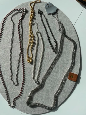 5 Mix av halsband i silver och guld - Säljer ett set med 5  halsband i olika stilar. Här finns både silverfärgade och guldfärgade kedjor, ett halsband med röda stenar och ett med små pärlor. Några halsband har detaljer som kulor och länkar. Perfekt för dig som gillar att variera din stil.